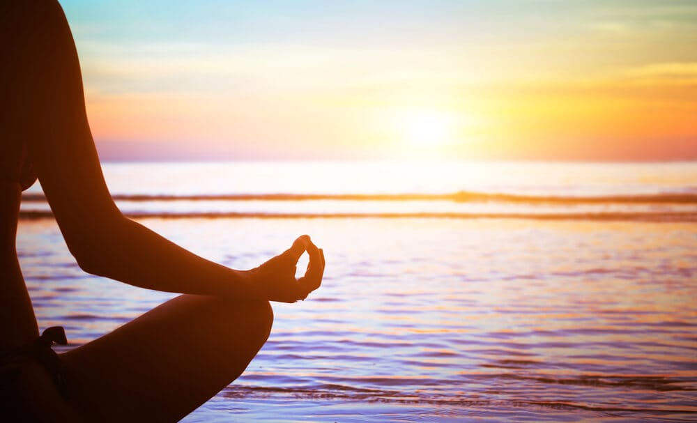 A person sits meditating in front of the ocean.