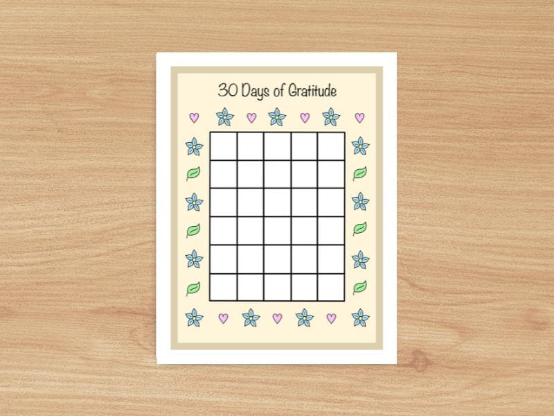 A piece of paper with the title "30 Days of Gratitude". It contains a central grid with 30 empty spots that is surrounded by hand drawn motifs of blue flowers, pink hearts and green leaves.