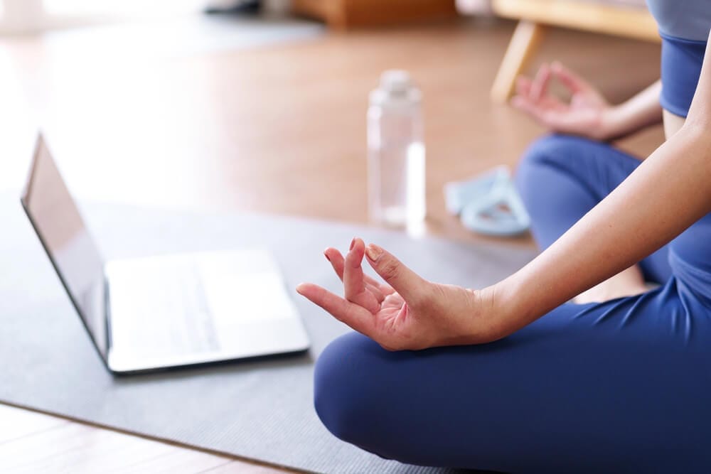 A woman meditating in front of a computer.