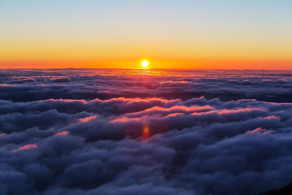 The yellow sun sets above grey clouds.