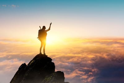 A woman stands on top of a mountain with her arms outstretched.